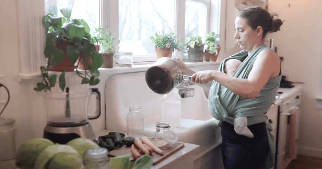 Woman pouring salt water brine from small saucepan to a large mason jar.